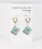 Pair of turquoise book-shaped earrings with gold accents on a white background, labeled 'Ear Sugar earrings'.