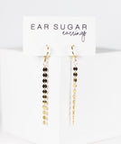 Pair of 'Ear Sugar' earrings on a white card with gold and black beads.