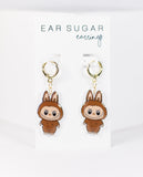 Pair of cartoon character earrings in a clear display case with 'Ear Sugar' branding.